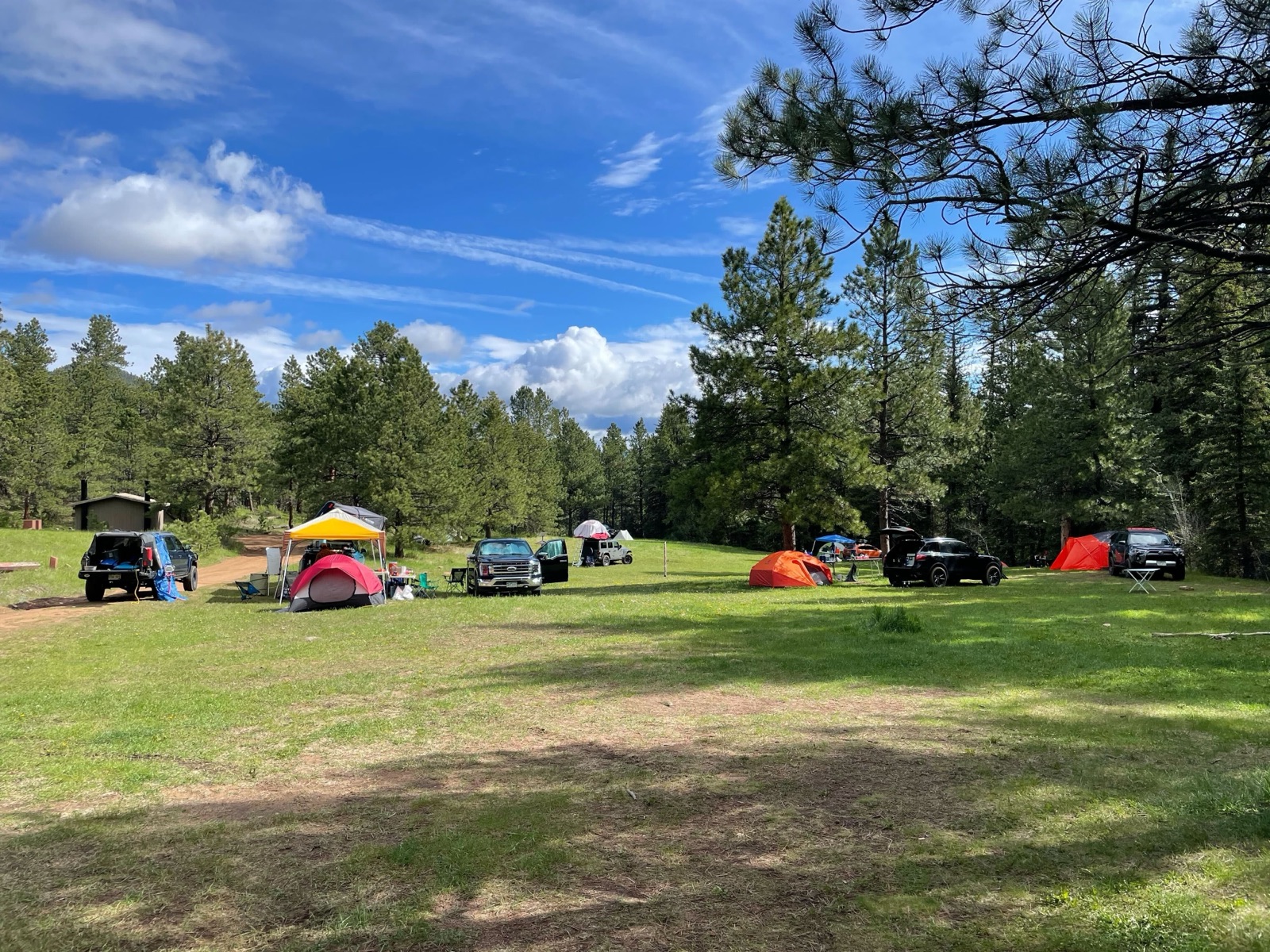 Tents and trucks spread across a sunny mountain meadow campsite