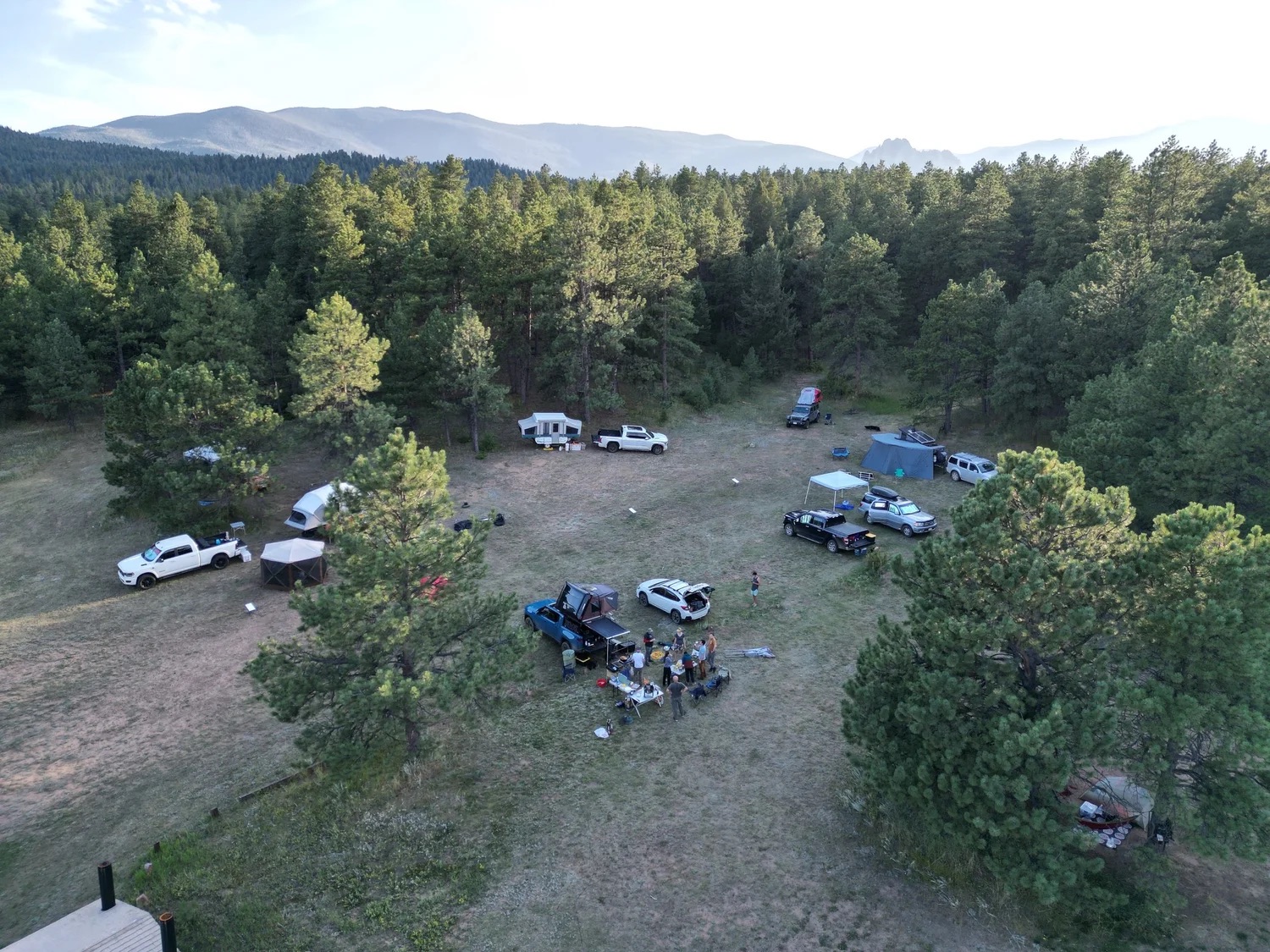 Aerial view of a Wild Spaces campsite in a forest clearing with mountains in the distance